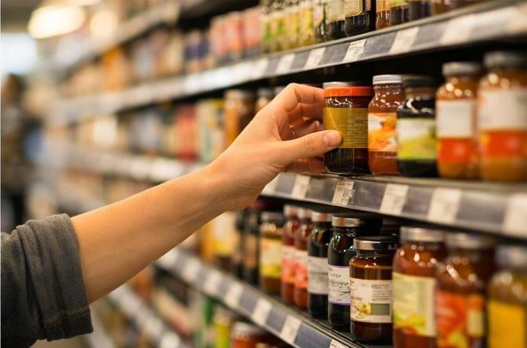 Рука тянется к баночке на полке продуктового магазина